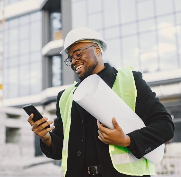 Young black race man with blueprint stading near glass building. Talking by phone.