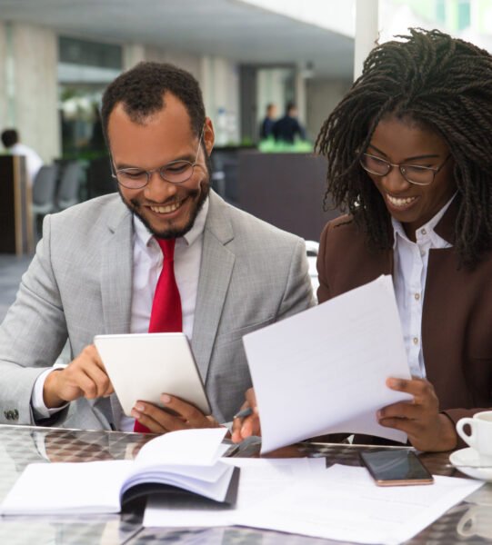 Cheerful business colleagues checking documents during coffee break. Business man and woman sitting in cafe, reading documents and using tablet. Paperwork concept