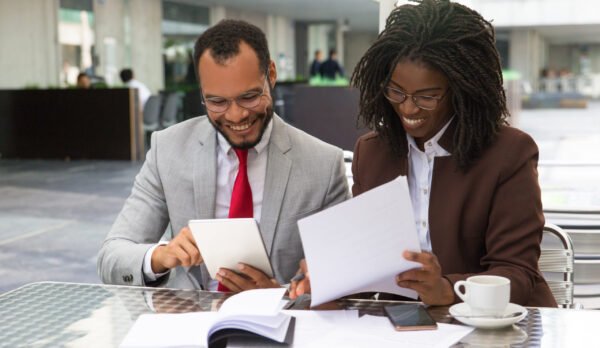 Cheerful business colleagues checking documents during coffee break. Business man and woman sitting in cafe, reading documents and using tablet. Paperwork concept